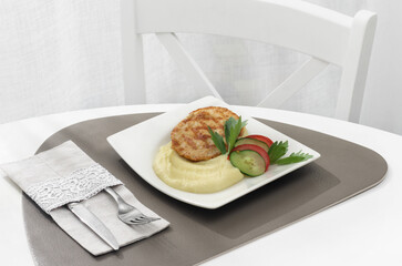 Two crispy meat or chicken cutlets in golden breading, served with mashed potatoes, fresh dill, cherry tomato on a white ceramic plate