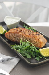 One piece of baked salmon grilled pepper lemon and salt on a brown plate with lettuce leaves