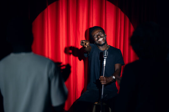Concept comedian show open mike. Happy young african american man comic performing standup monologue on stage with red curtains.