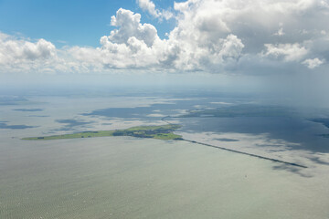 Aerial plane above image of the Dutch island, peninsula Marken, with iconic lighthouse and small historic village. Surrounded by former sea, not IJsselmeer, lake, under typical Holland cloud sky