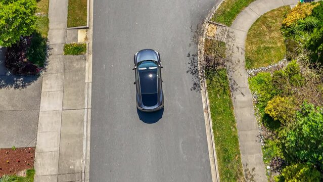 Title: Aerial view of a gray car driving through a suburban neighborhood arriving at home; drone follow shot