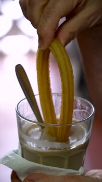 Slow motion. A person dips a churro into a glass of coffee