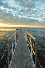 Fototapeta premium Vertical view of metallic walkway leading to wharf at sunrise on the Île aux Perroquets (Parrots Island) in the Mingan Archipelago National Park Reserve, Quebec, Canada