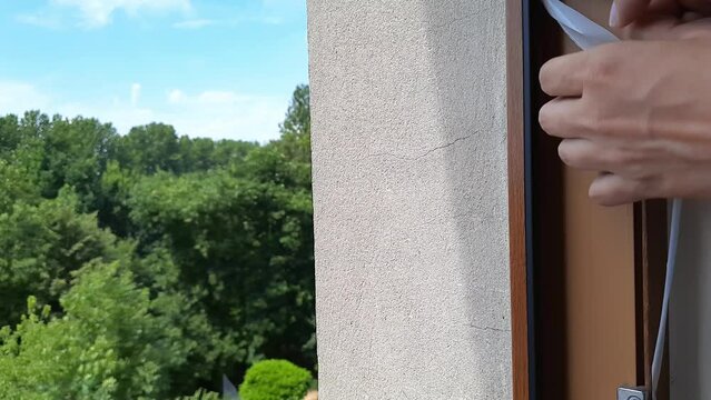Person applies adhesive tape to window frame before installing mosquito net. Preparing home for protection from insects, mosquitoes, flies, bees. Woman's hands close up. Prevention of insect bites