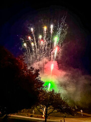 Green, pink, and silver fireworks streaking in to the sky above a neighborhood street