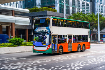 Double-decker city shuttle bus drives along route line among buildings on the street of a metropolis