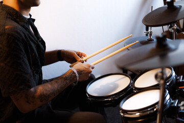 Partial shot of tattooed musician holding drum sticks near drums in music studio