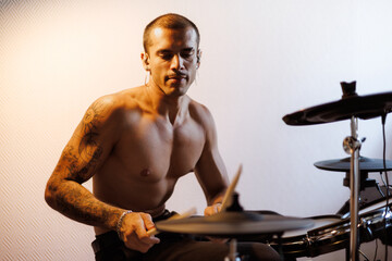 Tattooed man in in-ear monitors playing drums in studio