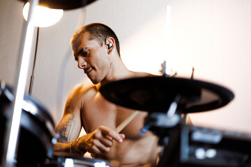 Muscular drummer in in-ear monitors playing electronic drums in studio