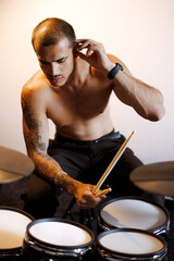 Shirtless mixed race drummer using ear monitors near drums in music studio