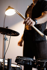 Partial shot of drummer holding drumsticks in music studio with lighting