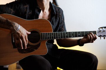 Obraz premium Partial view of tattooed musician playing acoustic guitar in music studio