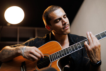 Obraz premium Portrait of tattooed man playing guitar in music studio