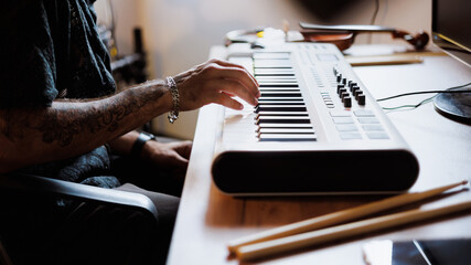 Partial shot of tattooed pianist playing synthesizer near drumsticks in music studio