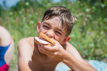 A little boy eats food on the beach after swimming