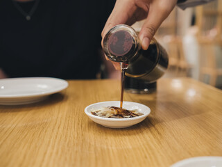 Hand Pouring Soy Sauce onto Shredded Ginger in Small Dish - Culinary Dining Experience