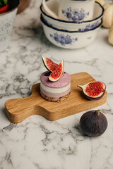 Healthy, vegan, raw, no-bake multi-layered, gluten-free dessert decorated with figs lies on a wooden small board on a marble background in the kitchen. Vertical shot, with no people