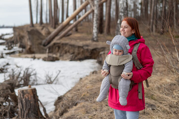 Caucasian red-haired woman walks with her son in an ergo backpack in nature in winter. 