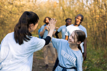 Cheerful woman doing high five with her daughter after finishing activity of clearing garbage and plastic waste, congratulating colleagues. Activist leader showing praise for a job well done.