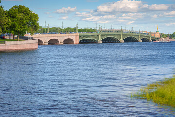 Fototapeta premium Panoramic view of Neva River, Trinity Bridge in background, In foreground is a coastline overgrown with grass, St Petersburg, Russia 