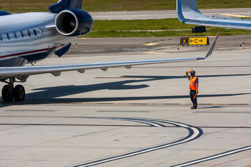 An air marshaller wearing an orange safety vest directing a commercial jet on a tarmac