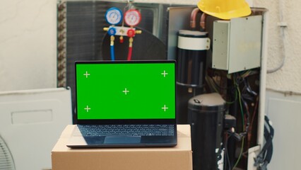 Green screen laptop in front of malfunctioning outdoor HVAC system. Mock up chroma key gadget display next to faulty condenser in need of professional refurbishing by specialists
