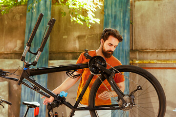 A fit young caucasian man repairs bike damage in home yard with professional repair-stand and...