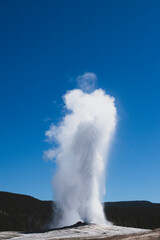 old faithful geyser eruption at Yellowstone National Park, with a clear sky.