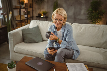 Obraz premium Mature woman work from home and use mobile phone on break drink coffee