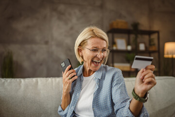 Fototapeta premium Mature senior woman buy online on mobile and use credit card on sofa