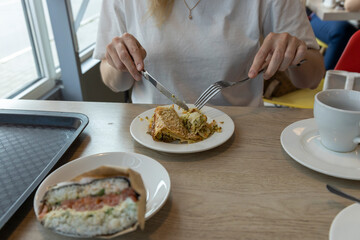 A person sits at a cafe table, enjoying a meal of savory crepes and sushi. They carefully slice the crepe with a knife and fork, savoring the flavors of this light and satisfying meal.