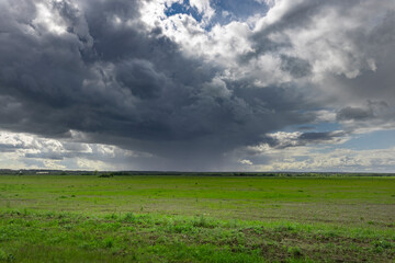 A large, green field under dark clouds. Rain threatens but the sun breaks through, casting a hazy...