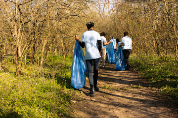 African american activist collecting trash and recycling in a blue bag, contributing to littler cleanup in the woods. Young girl doing voluntary work to protect the ecosystem.