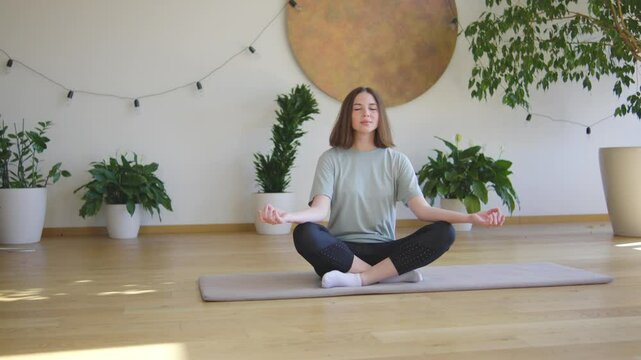 A woman is peacefully engaging in yoga and meditation at her home surrounded by indoor plants