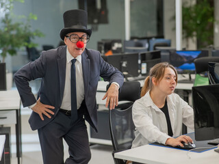 Caucasian woman works at the computer. Elderly man in clown costume in office. 