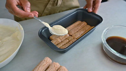 Person making tiramisu with ladyfingers and cream