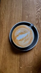 Coffee on a wooden counter with latte art in the shape of a leaf.