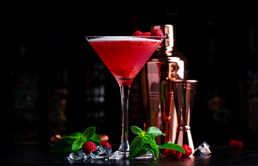 Summer red  cocktail with gin, raspberry syrup, lime juice, quail egg white and ice in glass. Black bar counter background