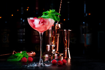 Raspberry cocktail with white rum, sugar syrup, fruit juice, lime, berry and ice in glass. Black bar counter background
