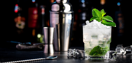 Gin cocktail drink with lime juice, syrup, soda, fresh mint and crushed ice. Black bar counter background