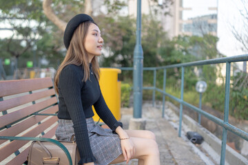 Tsim Sha Tsui, a woman in her twenties with black clothes, a beret, and a plaid mini skirt, sitting...
