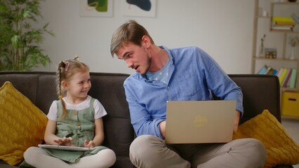 Obraz premium Shared Smiles: Father Shows Humorous Images to Daughter on Sofa