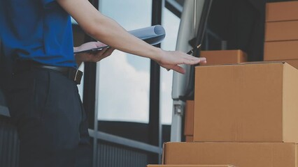 Young cheerful delivery man with parcel near car full of cardboard boxes, full length shot. Shipping service concept