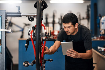 Bike repair, maintenance and tablet with mechanic in workshop for frame building or professional engineering. Assessment, bicycle and transport with man technician in small business for restoration