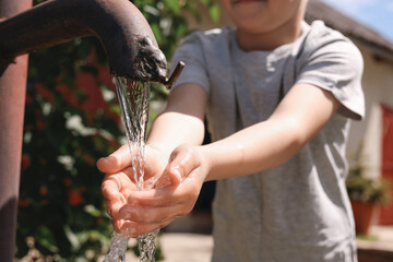 Water scarcity. Little boy drawing water with hands from tap outdoors, closeup