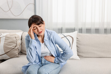 Upset woman suffering from headache on sofa at home