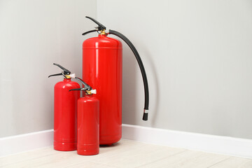 Obraz premium Fire extinguishers on floor near light grey wall, space for text