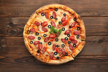 Tasty pizza with dry smoked sausages, tomato, olives, pepper and parsley on wooden table, top view