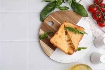 Pieces of toasted bread with melted cheese, tomatoes and basil on white tiled table, top view. Space for text