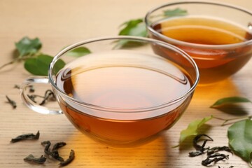 Refreshing green tea in cups and leaves on wooden table, closeup